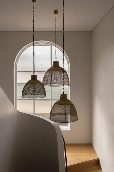Stair void with pendant lights before an arched window, Cottesloe